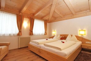 Een kamer met een houten plafond, twee bedden met witte beddengoed, een houten nachtkastje en een radiator.