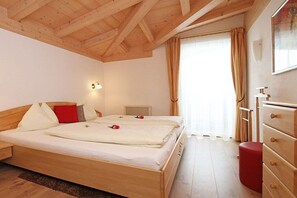 A bedroom with a wooden bed, a dresser, and a window with curtains. - Holiday apartment with 1 bedroom (Leogang)
