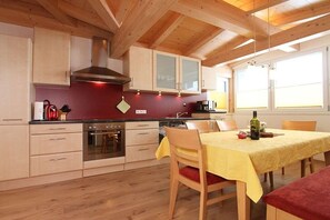 A kitchen with wooden cabinets, a stove, and a dining table set for two. - Holiday apartment with 1 bedroom (Leogang)