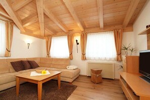Een gezellige woonkamer met een houten plafond, een bank, een salontafel, een tv-meubel en gordijnen.