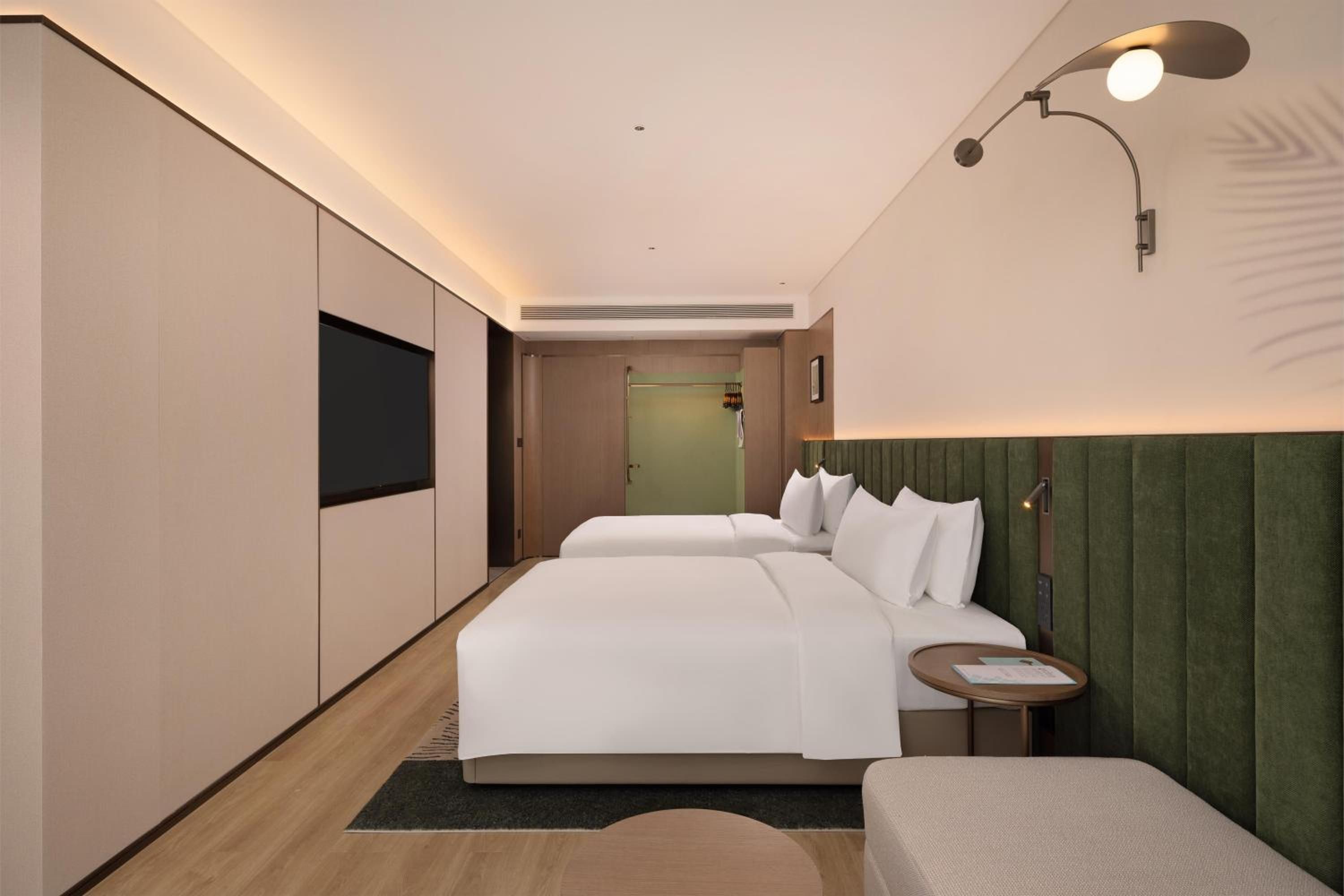 A hotel room with two beds, a flat-screen TV, a bedside table, and a wall-mounted lamp.