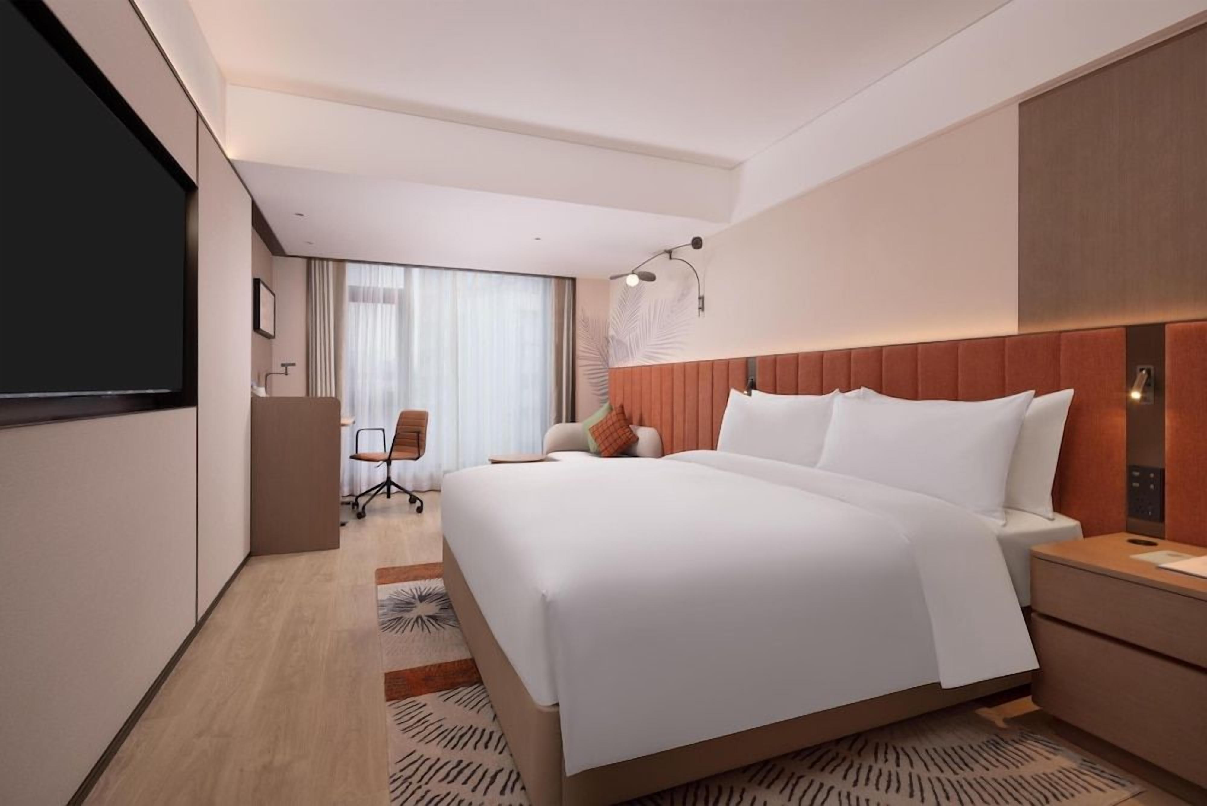 Une chambre d’hôtel avec un grand lit, un bureau, une chaise, une télévision et une fenêtre avec des rideaux.