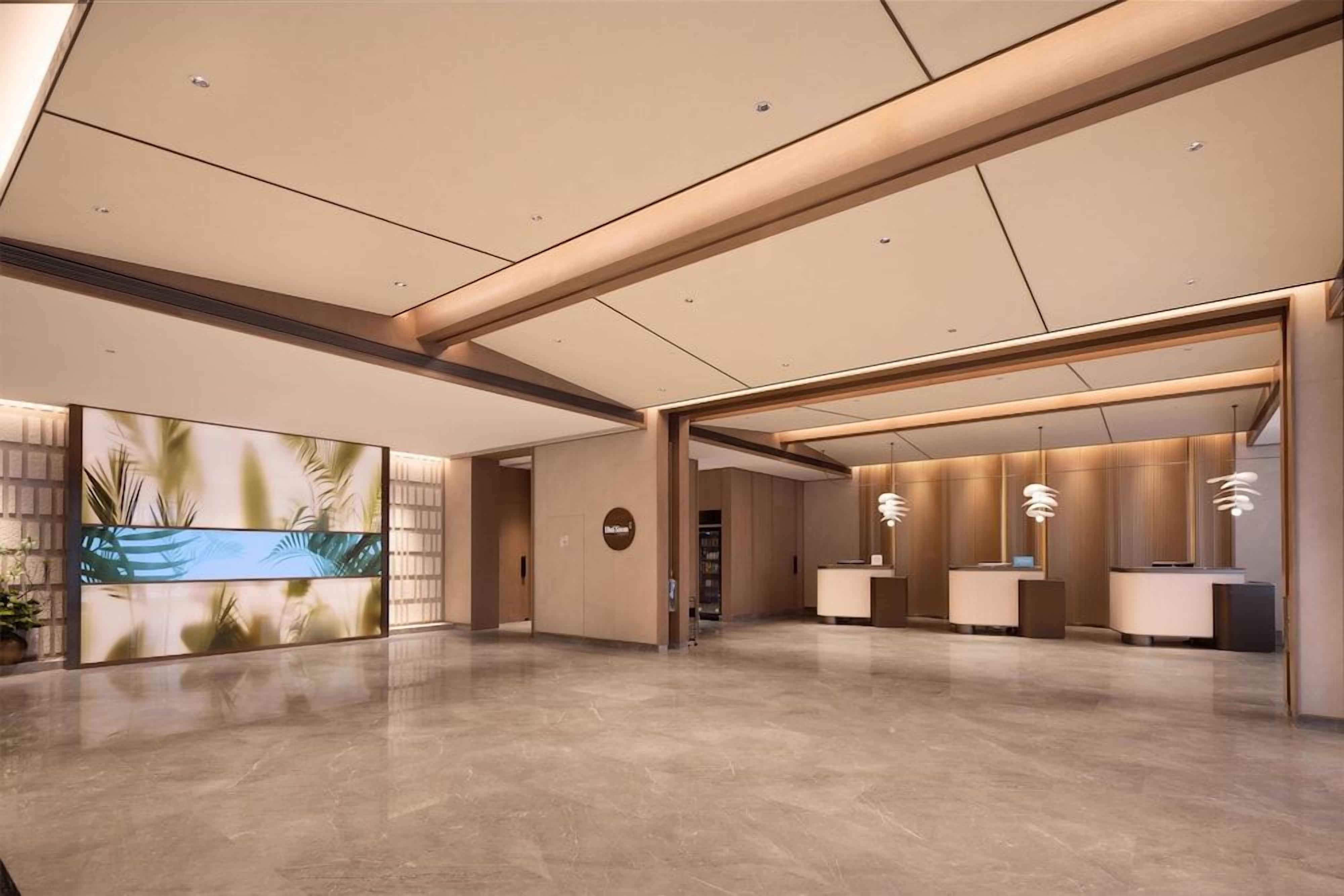 A spacious lobby with a reception desk, a large digital display, and a modern ceiling design.