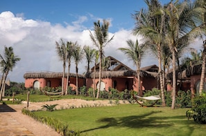 A resort with thatched-roof buildings, palm trees, and a hammock in the garden. - Joud by the Sea Zanzibar (Jambiani)