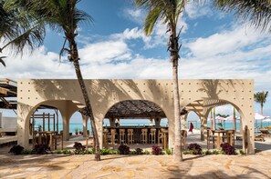 A beachside bar with outdoor seating, palm trees, and a view of the ocean. - Joud by the Sea Zanzibar (Jambiani)