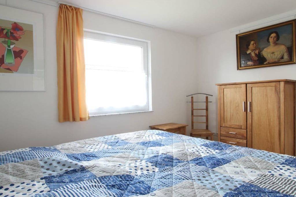 Une chambre à coucher avec un lit, une fenêtre avec des rideaux, une armoire en bois et un tableau accroché au mur.