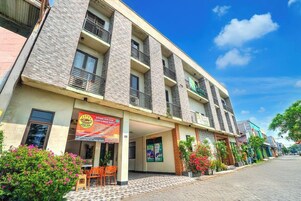 Un hotel de varios pisos con entrada de baldosas, asientos al aire libre y un letrero.