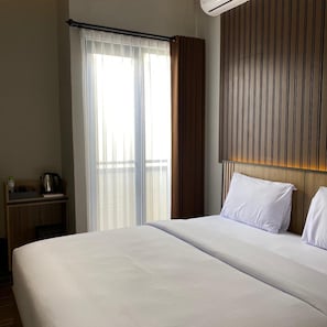 A hotel room with a bed, a nightstand, a kettle, and a window with curtains. - Moonstone (Bandung)