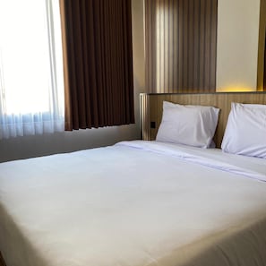 A hotel room with a large bed, a wooden headboard, and a window with curtains. - Moonstone (Bandung)