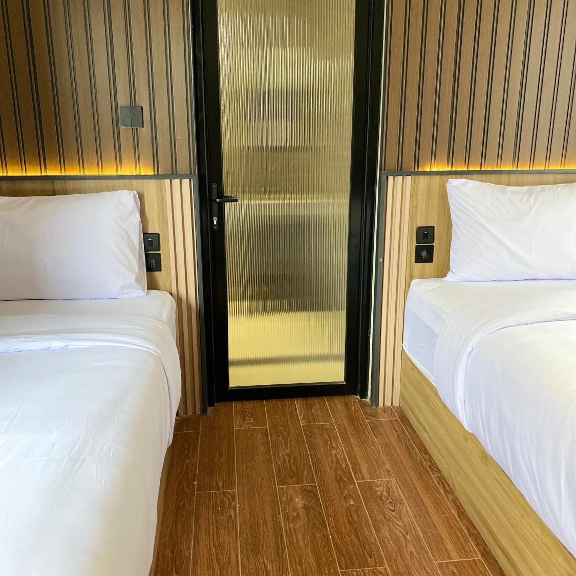 Hotellihuone, jossa on kaksi sänkyä, puulattia ja ovi, jossa on pystysuorainen raidallinen kuvio.