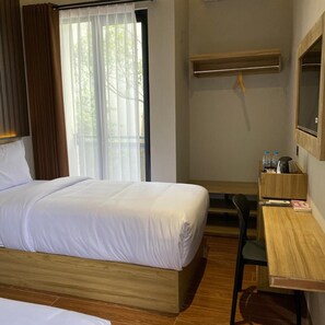 A hotel room with a bed, a desk, a chair, a mirror, and a window with curtains. - Moonstone (Bandung)