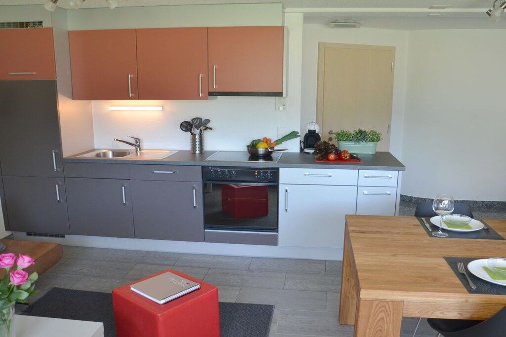 Eine kompakte Küche mit grauen und orangefarbenen Schränken, einem eingebauten Backofen und einem Essbereich mit Holztisch und Stühlen.