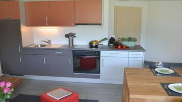 Eine kompakte Küche mit grauen und orangefarbenen Schränken, einem eingebauten Backofen und einem Essbereich mit Holztisch und Stühlen.