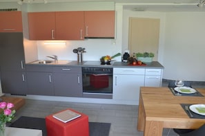 Una cocina compacta con armarios grises y anaranjados, horno empotrado y comedor con mesa y sillas de madera.