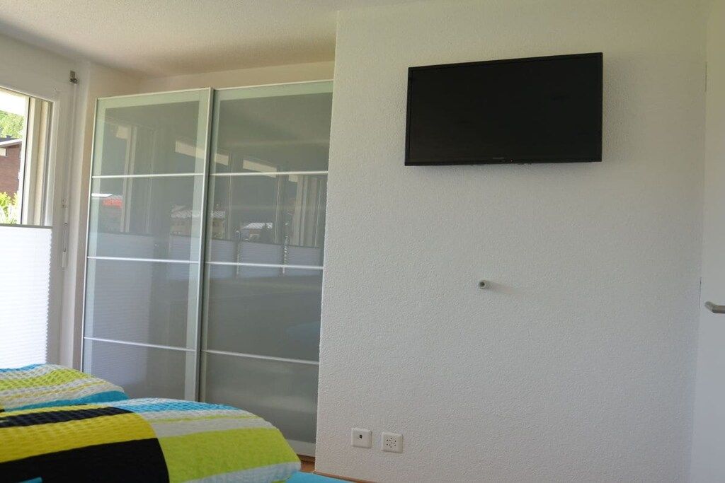 Une chambre à coucher avec un lit, une porte-fenêtre coulissante et un téléviseur fixé au mur.