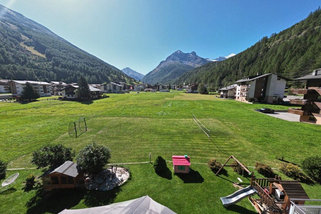 Un quartier résidentiel avec des maisons, un champ verdoyant et des montagnes en arrière-plan.