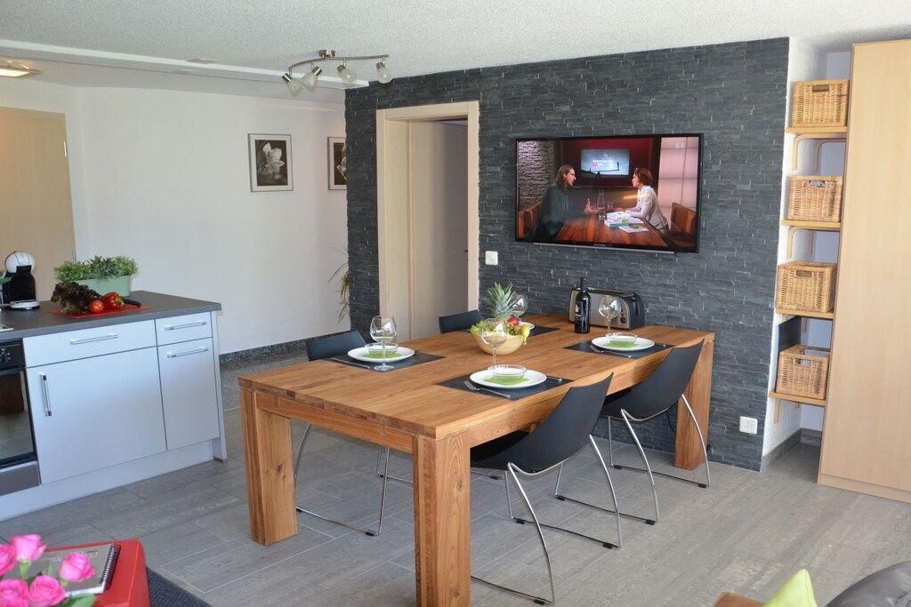 Een moderne keuken met een eethoek, een flatscreen televisie bevestigd aan een stenen muur, en een houten eettafel met stoelen.