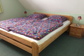 A single-bed room with a wooden frame, a colorful bedspread, a bedside table with a lamp, and a small drawer. - Holiday home in Glowe with swimming pool (Glowe)
