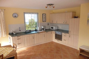 A kitchen with light-colored cabinets, a microwave, a sink, and a window with curtains. - Holiday home in Glowe with swimming pool (Glowe)