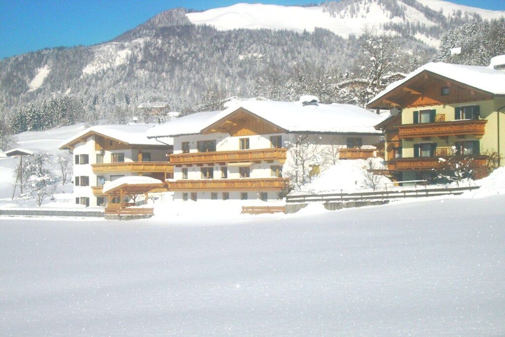 A snow-covered building with multiple balconies, likely a hotel or lodge, set against a mountainous backdrop.