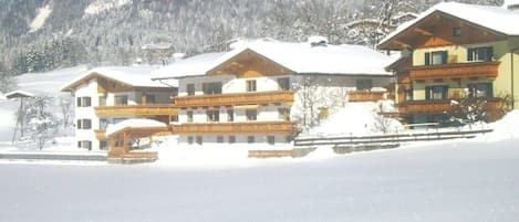 A snow-covered building with multiple balconies, likely a hotel or lodge, set against a mountainous backdrop.