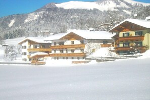 Ein schneebedecktes Gebäude mit mehreren Balkonen, vermutlich ein Hotel oder eine Pension, vor einer Bergkulisse.