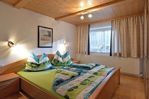 Ein Schlafzimmer mit einem hölzernen Bett, einem Nachttisch, einem gerahmten Bild an der Wand und einem Fenster mit Vorhängen.