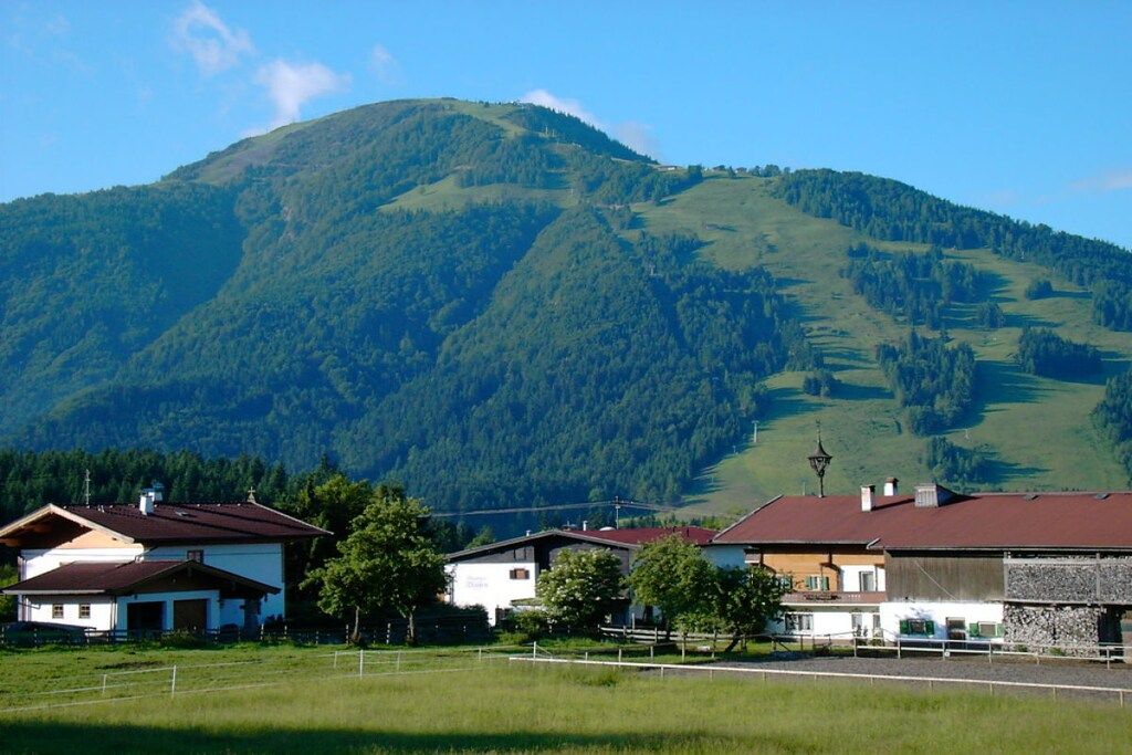 A rural setting with a mountain in the background, houses with red roofs, and a clear sky.