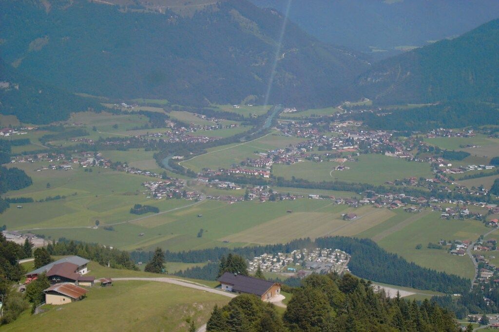 A rural landscape with a small village, surrounded by green fields and mountains.