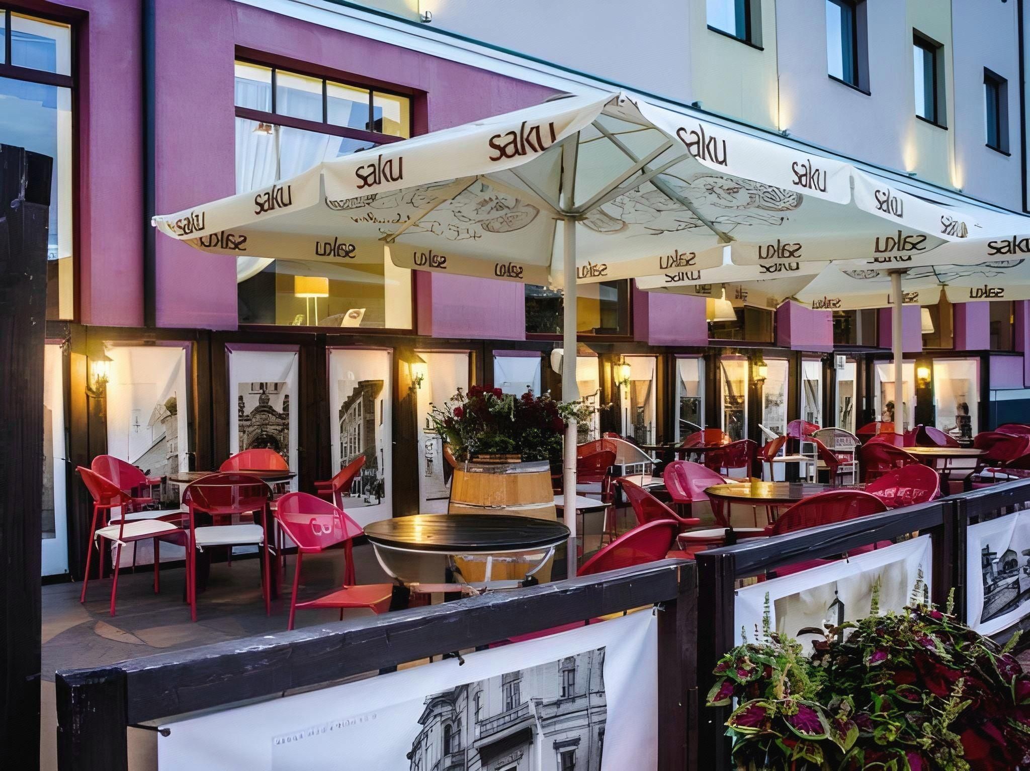 An outdoor seating area with red chairs and tables, covered by umbrellas with the name 'Saku'.