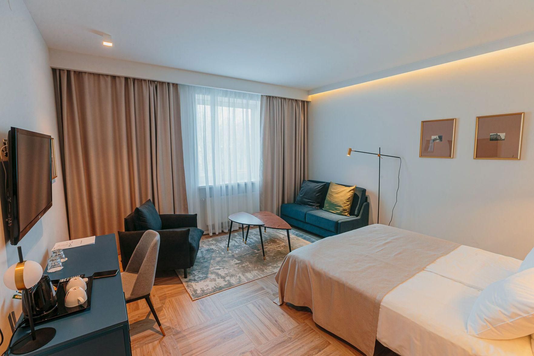 A hotel room with a bed, a desk with a chair, a sofa, a coffee table, and a TV.