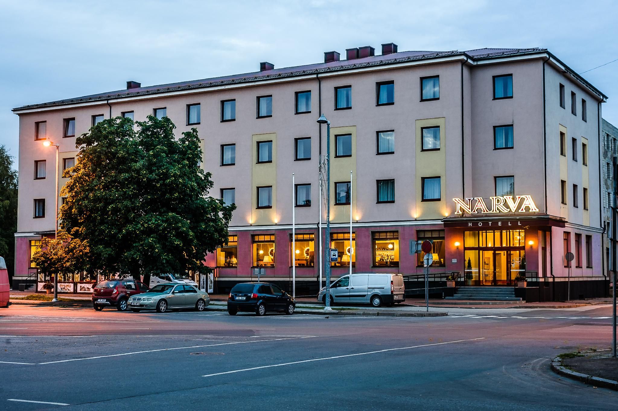 A hotel with a flat facade, multiple windows, and a sign that reads 'NARVA HOTEL'.