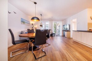 Eine moderne Küche mit Holzausstattung, ein Essbereich mit rundem Tisch und Stühlen sowie ein großes Fenster für natürliches Licht.