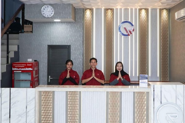 Un mostrador de recepción con tres personas detrás, un reloj y una puerta al fondo.