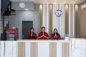 A reception desk with three individuals standing behind it, a clock, and a door in the background.