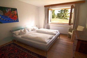 A bedroom with a bed, a chair, a desk, a window with curtains, and a painting on the wall. - Holiday apartment in Telfes with sauna (Telfes)