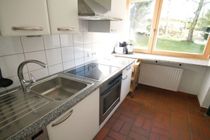 A kitchen with white cabinets, a stainless steel sink, a built-in oven, and a window overlooking a garden. - Holiday apartment in Telfes with sauna (Telfes)
