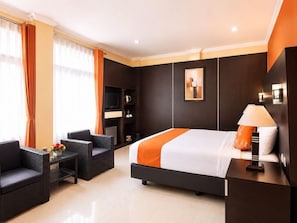 Quarto de hotel com cama, duas poltronas, uma mesinha, televisão e abajur.