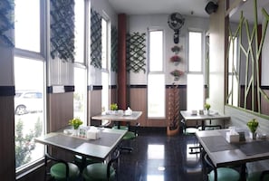 A restaurant with tables and chairs, a decorative wall, and a view of the street. - Akasia Budget Hotel (Promong)
