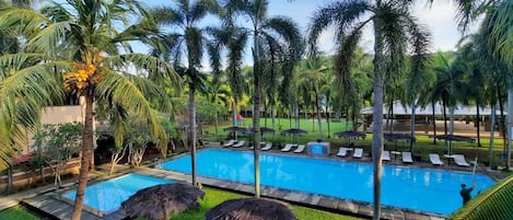 Zona de piscina con sillones de descanso y palmeras.
