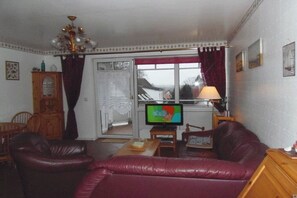 Een woonkamer met een televisie, leren bank, houten kast en een raam met gordijnen.