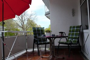 A balcony with a red umbrella, two plaid chairs, a small table with a potted plant, and a metal railing. - Holiday apartment with 2 bedrooms (Zinnowitz)