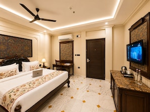 Una habitación de hotel con cama, escritorio, silla, televisor y ventilador de techo.