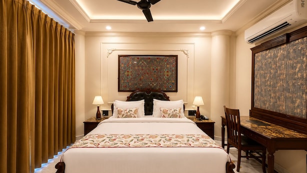 Quarto de hotel com cama, mesas de cabeceira, escrivaninha, cadeira, ventoinha no teto e ar condicionado.