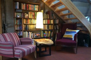A cozy reading nook with a striped sofa, a chair, a small table, and a large bookshelf filled with books. - Timber-framed house Melz (Melz)