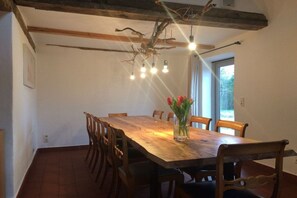 A dining area with a wooden table and chairs, a chandelier, and a window with natural light. - Timber-framed house Melz (Melz)