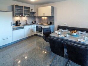 A modern kitchen with white cabinets, a built-in oven, and a dining area with a table set for two. - Holiday Home With 1 Bedroom (Esens)