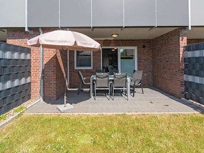 An outdoor patio with a table and chairs, a covered seating area, and a brick building in the background. - Holiday Home With 1 Bedroom (Esens)