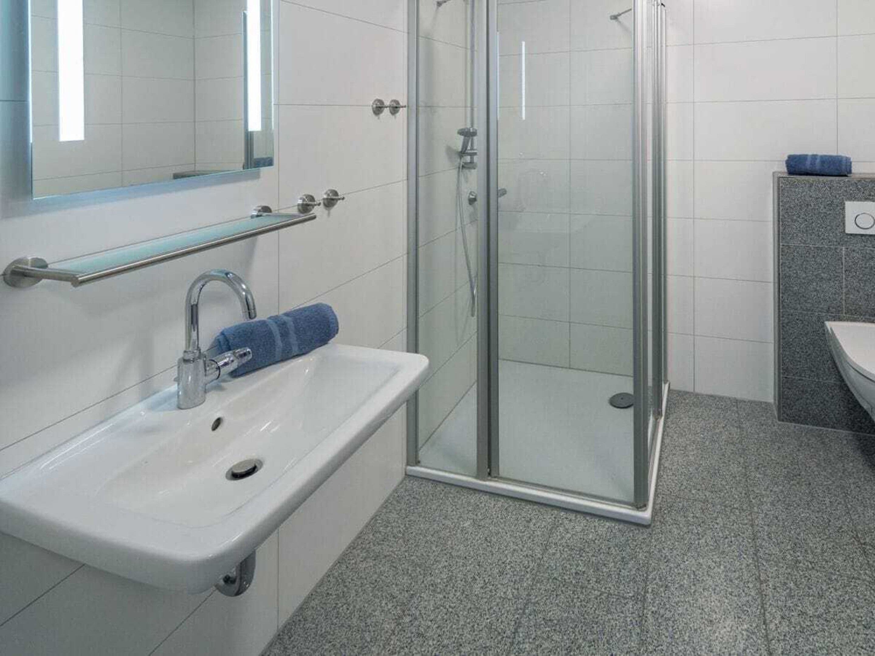 Ein Badezimmer mit Duschkabine aus Glas, einem weißen Waschbecken mit Handtuch und einem Spiegel darüber.