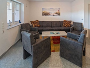 Ein Wohnzimmer mit einem Ecksofa, zwei Sesseln, einem Couchtisch und einem Gemälde an der Wand.